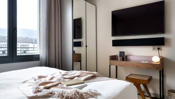 Quarto de hotel moderno com uma cama grande, uma escrivaninha com abajur, televisão de tela plana e vista para edifícios pela janela.