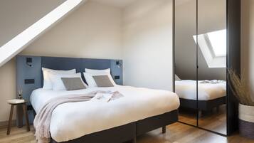 Une chambre moderne avec un grand lit, une lucarne et un placard avec des portes miroir.