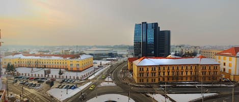Un paisaje urbano con un edificio moderno destacado, una glorieta y edificios circundantes de color amarillo.