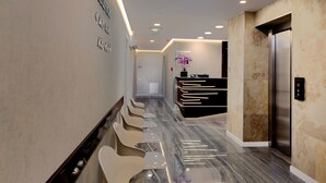 Un moderno vestíbulo de hotel con suelo de mármol, una recepción y una fila de sillas blancas.
