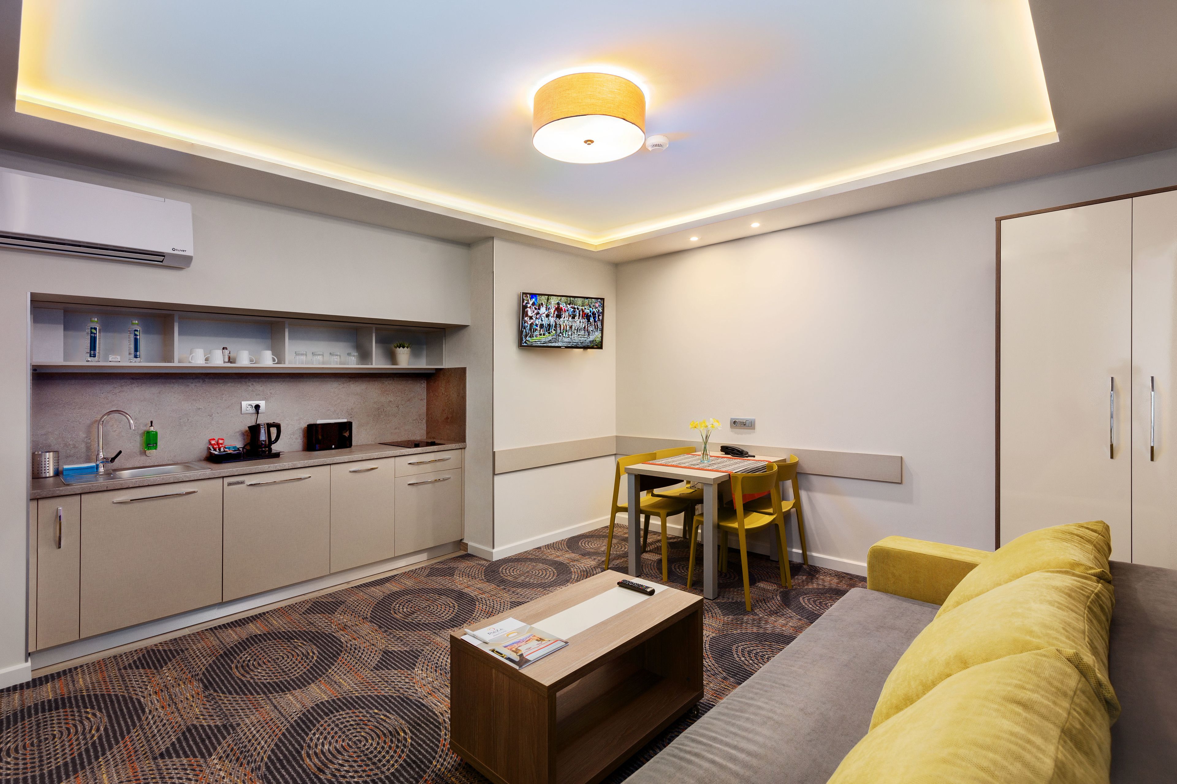 Una habitación de hotel moderna con kitchenette, zona de comedor y sofá.
