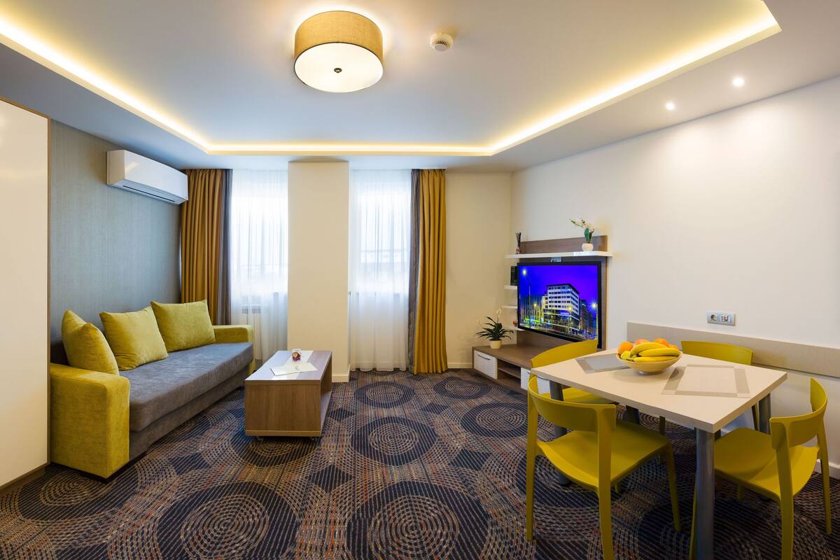 A modern hotel room with a sofa, a dining table, and a TV.