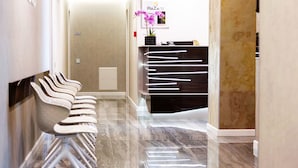 Un área de recepción de diseño moderno, con piso de mármol, una recepción de acabado oscuro y una fila de sillas blancas a la izquierda.