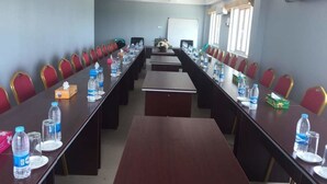 Une salle de conférence dotée de longues tables et de chaises rouges, ainsi que de bouteilles d’eau et de boîtes de mouchoirs.