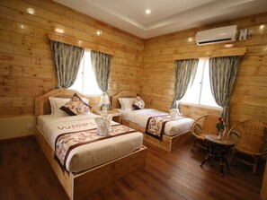Quarto estilo cabana de madeira com duas camas, uma mesinha e uma cadeira.