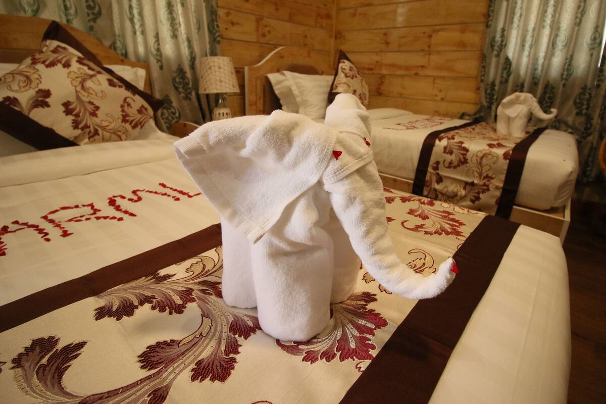 A hotel room with a wooden interior, a bed with floral bedding, a nightstand with a lamp, and a towel shaped like an elephant.