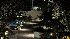 A nighttime pathway leading to a building with a palm tree and a blue umbrella.