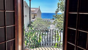 Una porta in legno aperta che dà su un balcone con vista sul mare e una palma.
