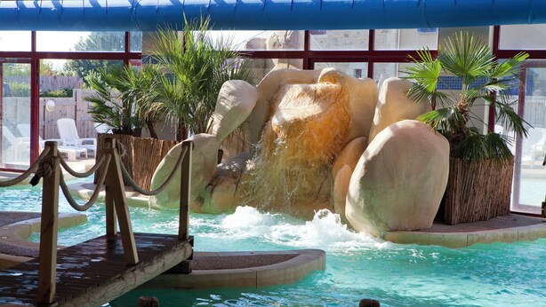 A pool with a waterfall feature, surrounded by lounge chairs and potted plants. - Le Village Cancalais (Cancale)