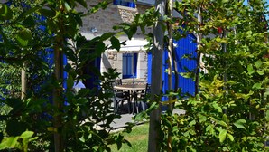 A stone building with blue shutters and a wooden table and chairs in the foreground. - Le Village Cancalais (Cancale)