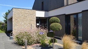 A modern building with a stone facade, large windows, and a well-maintained garden with various plants and flowers. - Le Village Cancalais (Cancale)