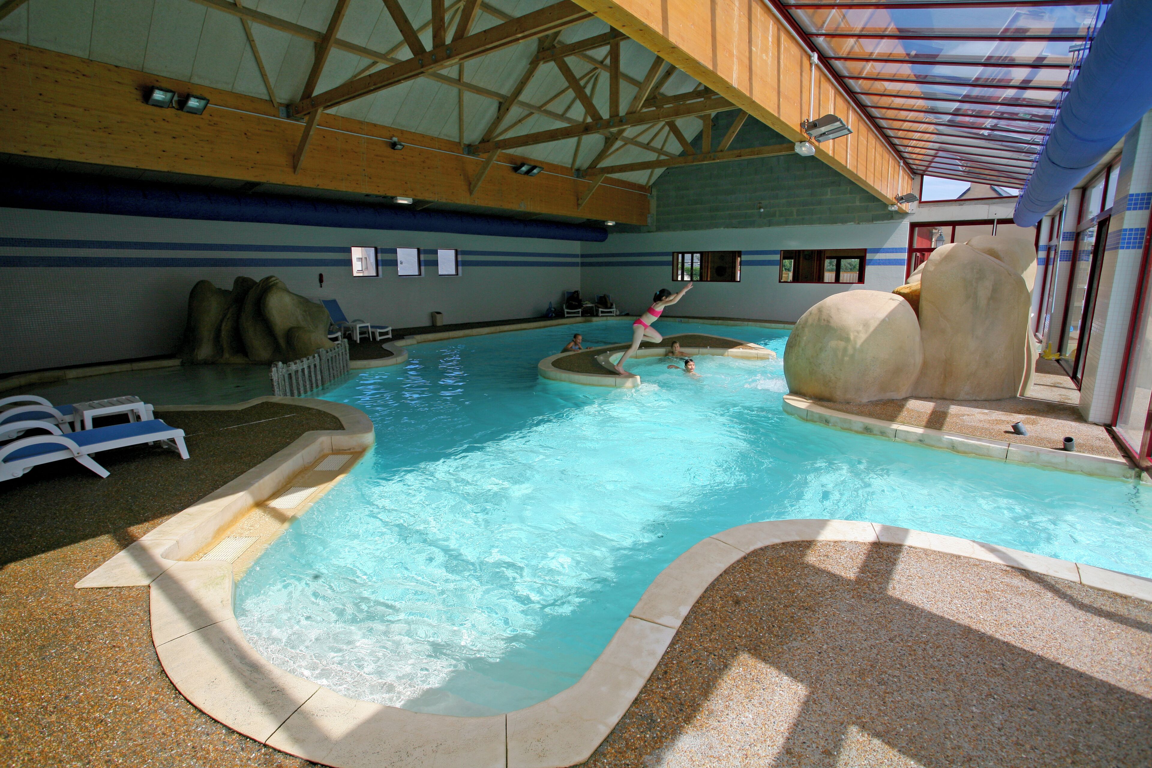 An indoor swimming pool with a wooden ceiling, clear water, and a few people swimming.