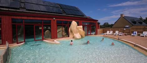 Una piscina con una gran formación rocosa, rodeada por un edificio de amplios ventanales y fachada roja.