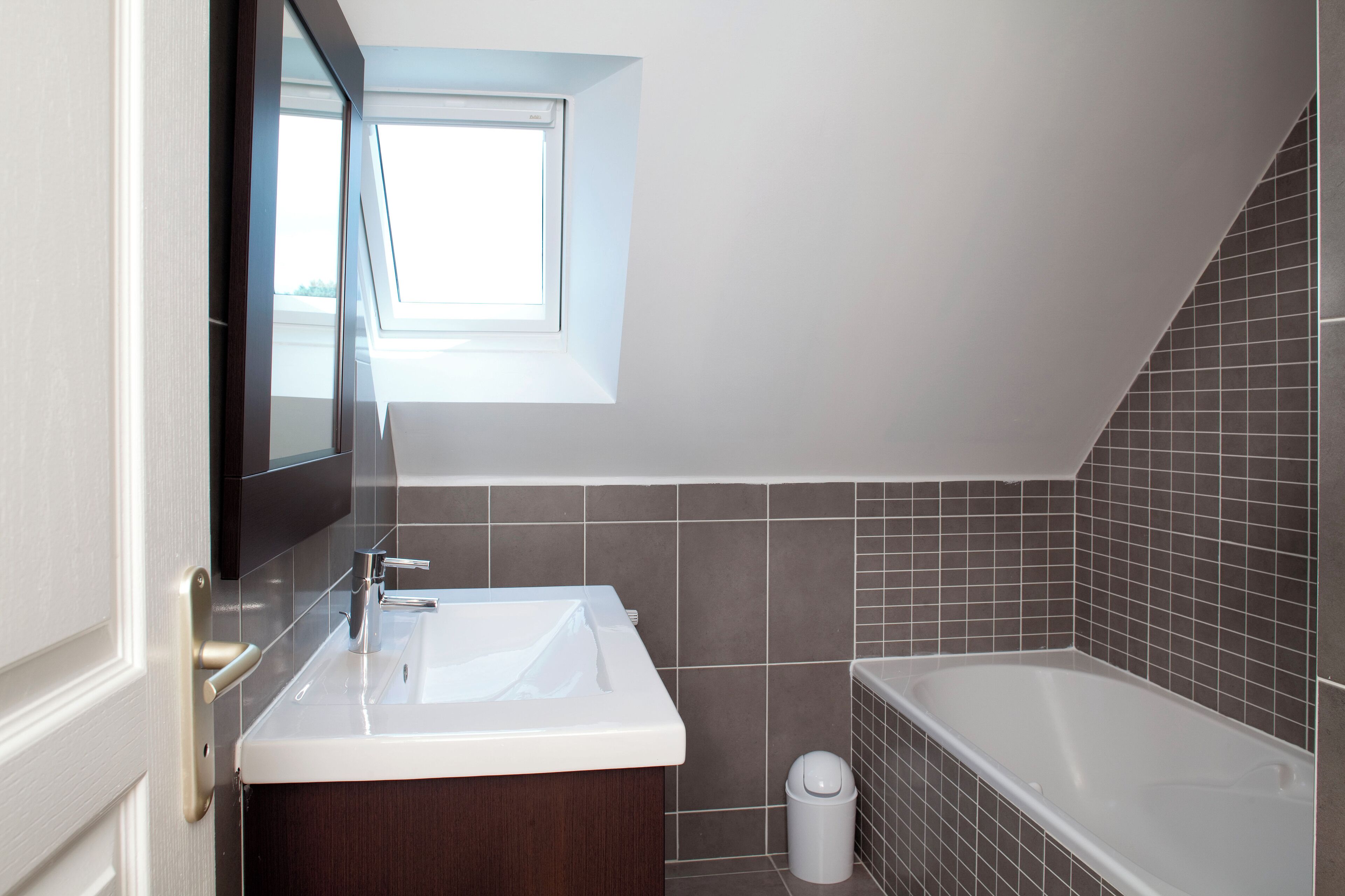 Un bagno moderno con una finestra a lucernario, una vasca e un mobile lavabo con specchio.