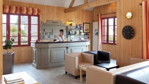 A wooden interior with a reception desk, seating area, and a clock on the wall. - Le Village Cancalais (Cancale)