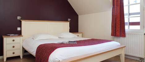 A bedroom with a bed, nightstands, a window with curtains, and a sloped ceiling.