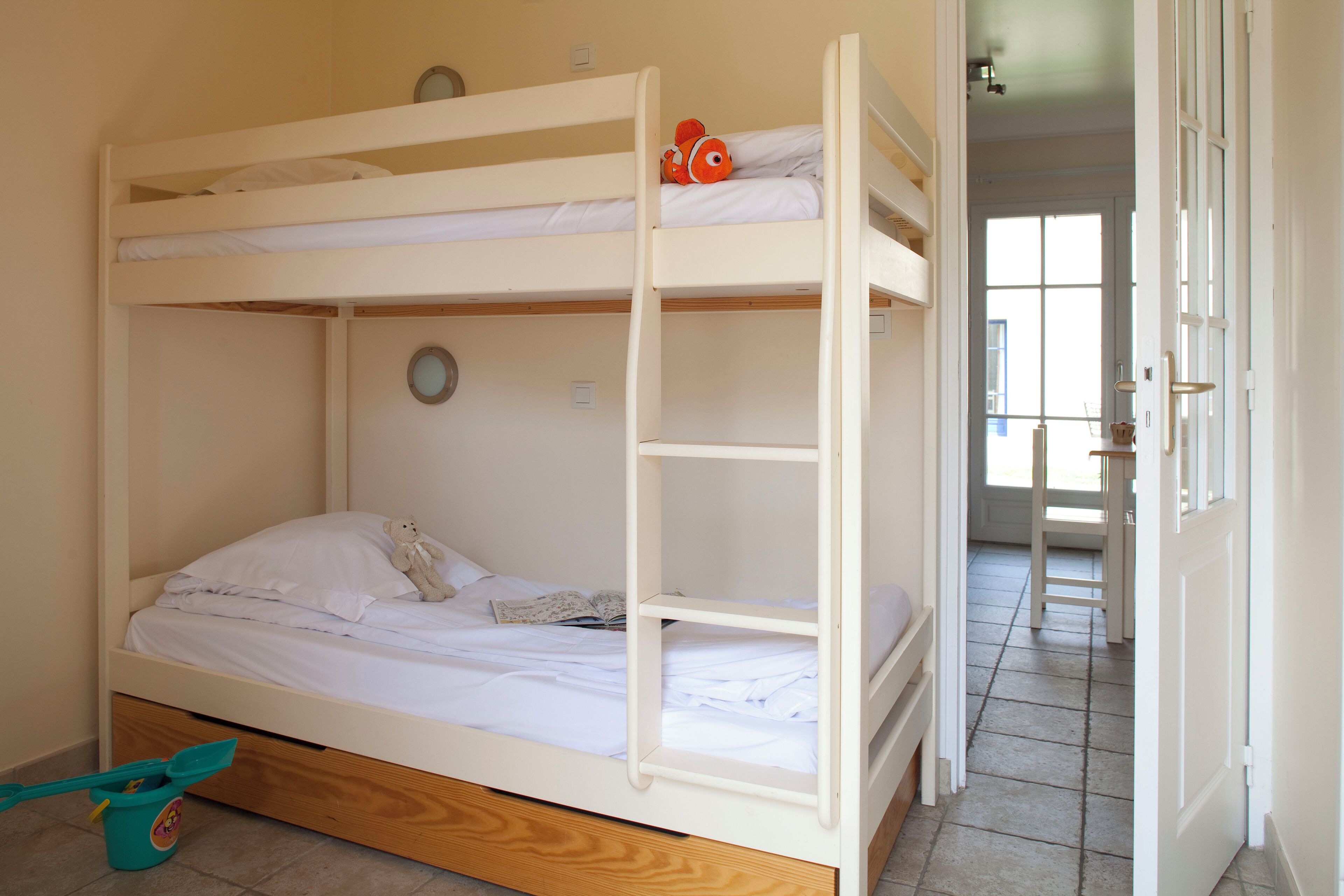Een stapelbed met een speelgoedvis op het bovenste bed, een teddybeer beneden en een ronde klok aan de muur.