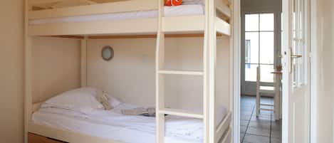 Una cama litera con un pez de juguete en la parte superior, un oso de peluche en la inferior y un reloj redondo pequeño en la pared.