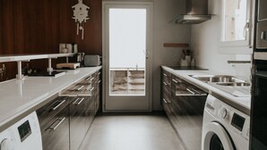 A modern kitchen with white countertops, wooden cabinets, a built-in washing machine, and a large window. - Stunning ski & walking chalet with best views in Wengen (Lauterbrunnen)