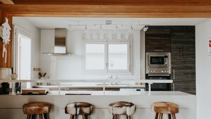 A modern kitchen with a central island, bar stools, a stainless steel range hood, and a microwave. - Stunning ski & walking chalet with best views in Wengen (Lauterbrunnen)