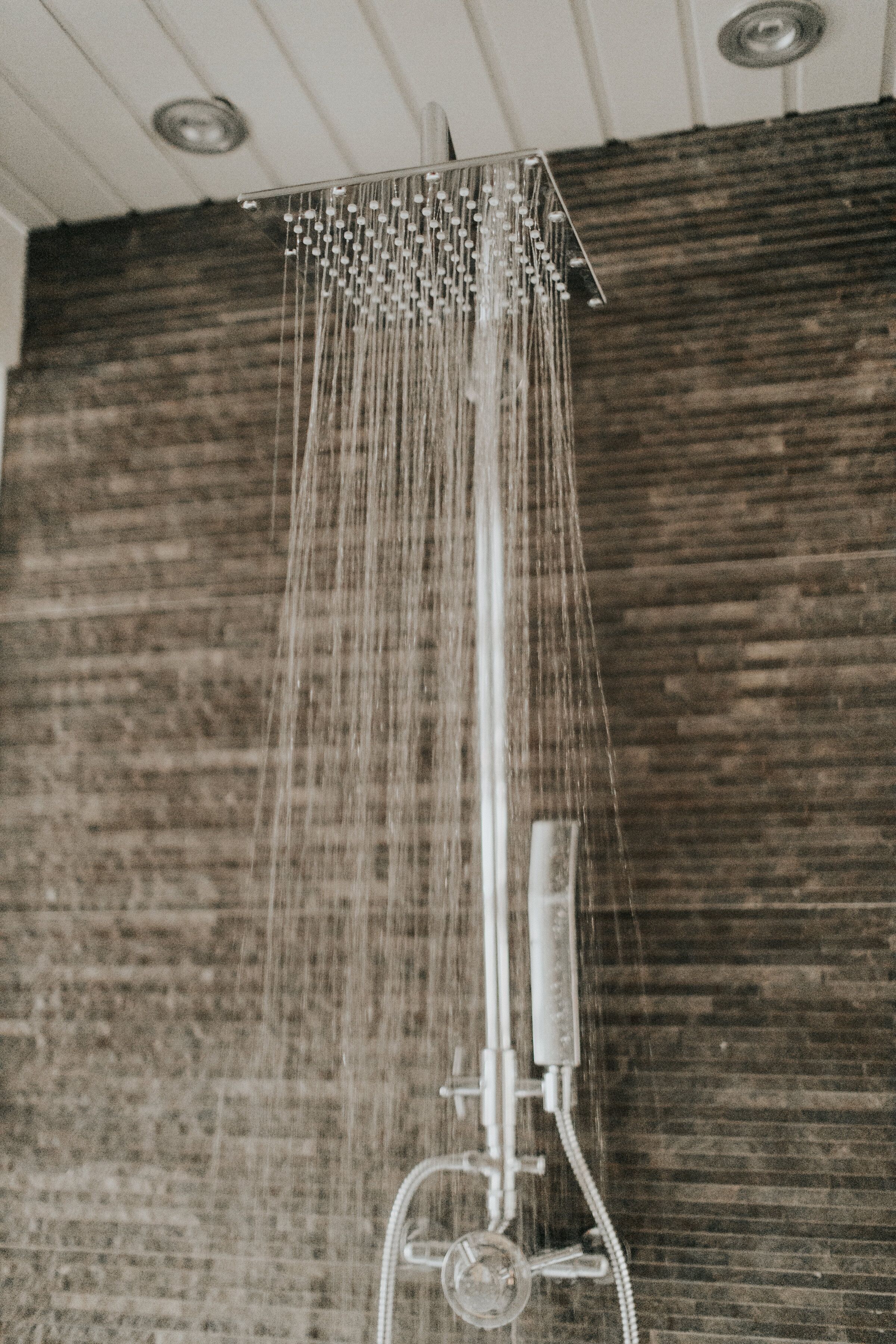A shower with multiple nozzles, a control panel, and a wooden wall in the background.