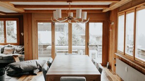 A wooden interior with a large dining table, chairs, a chandelier, and large windows. - Stunning ski & walking chalet with best views in Wengen (Lauterbrunnen)