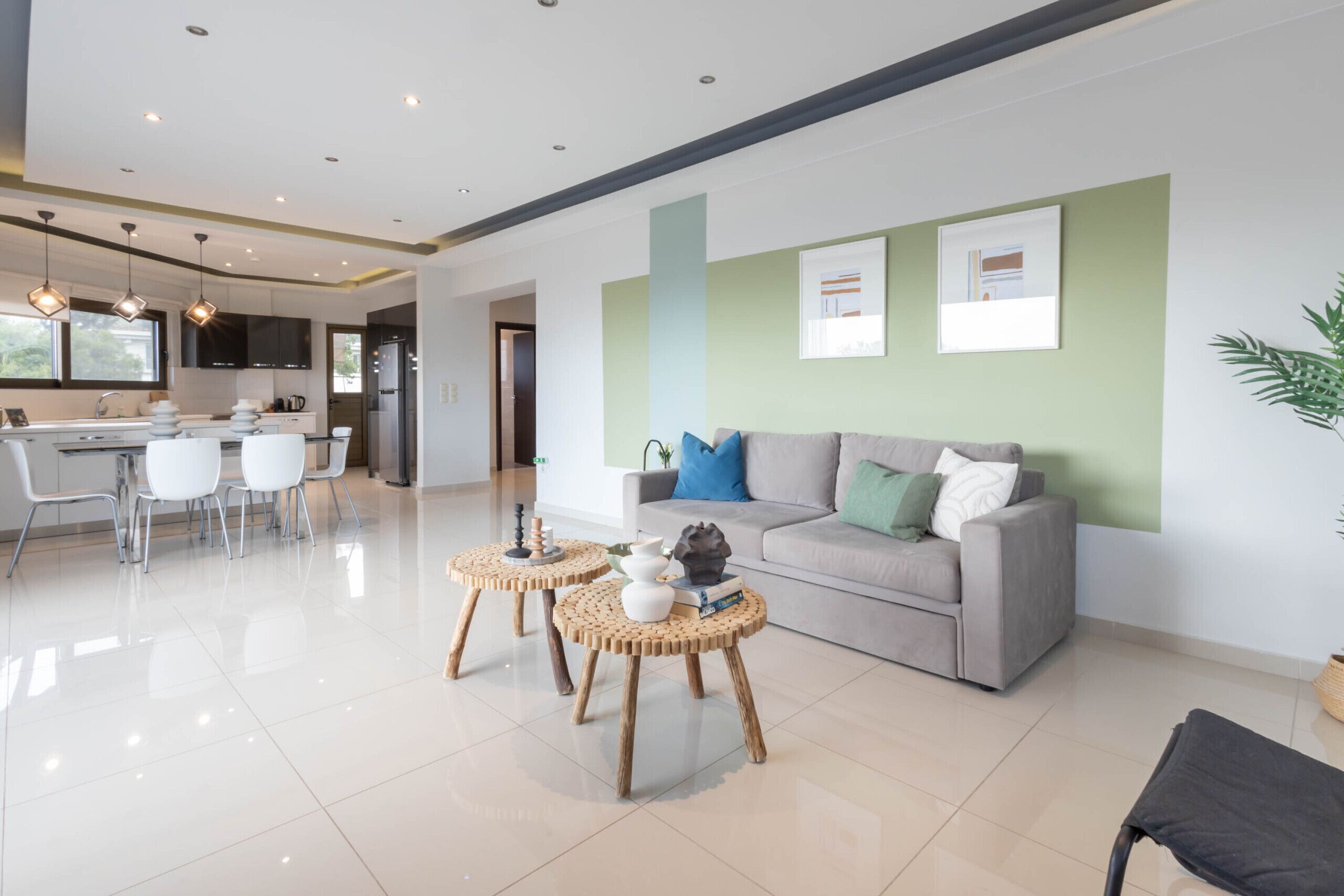 A modern living room with a grey sofa, two round wooden tables, and a kitchen in the background.