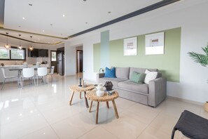 A modern living room with a grey sofa, two round wooden tables, and a kitchen in the background.