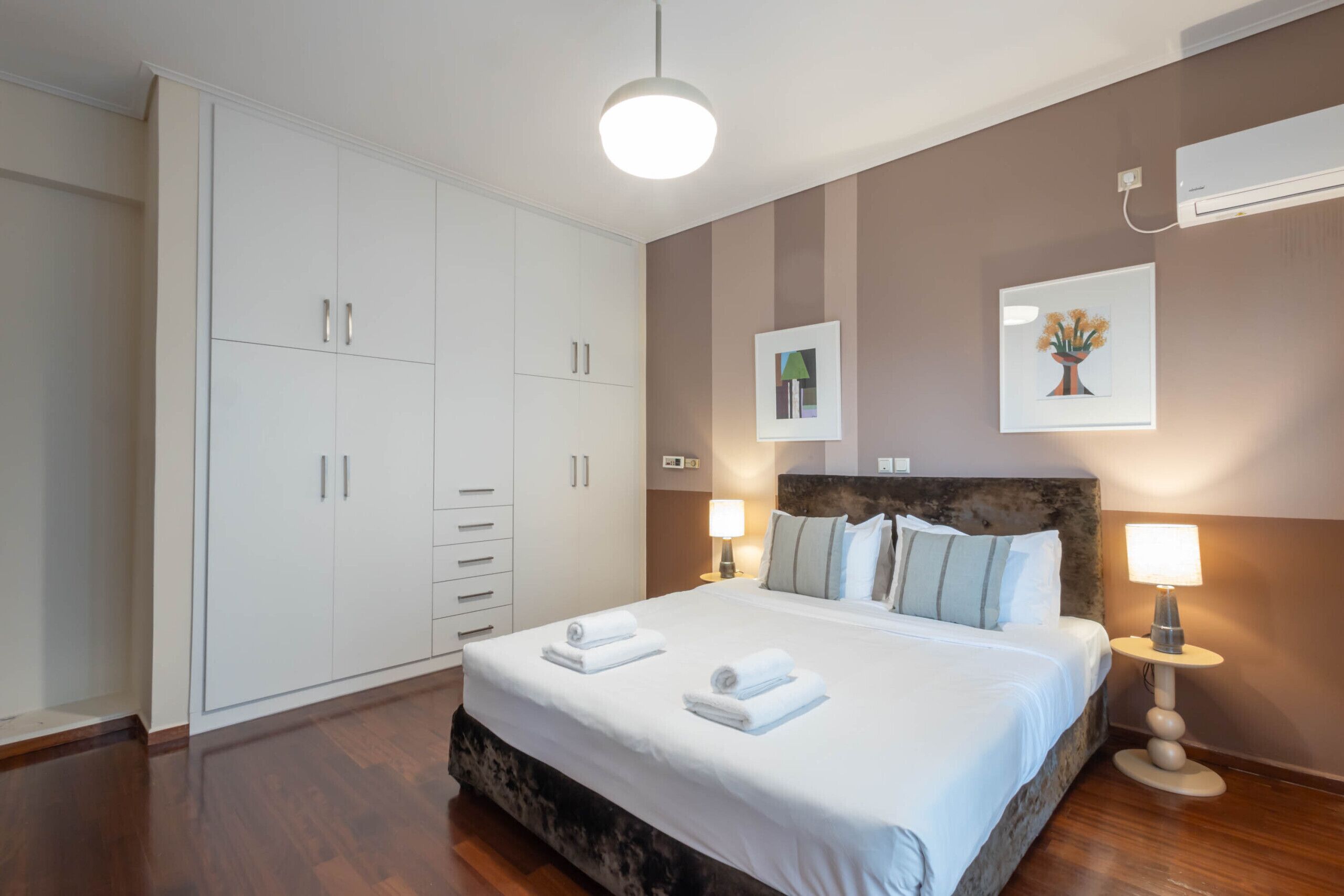 Een slaapkamer met een groot bed, nachtlampjes, een kledingkast en een wandairconditioner.
