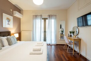 Ett hotellrum med en säng, ett sängbord, en stol, ett skrivbord, en spegel, en TV, en luftkonditioneringsanläggning och gardiner.