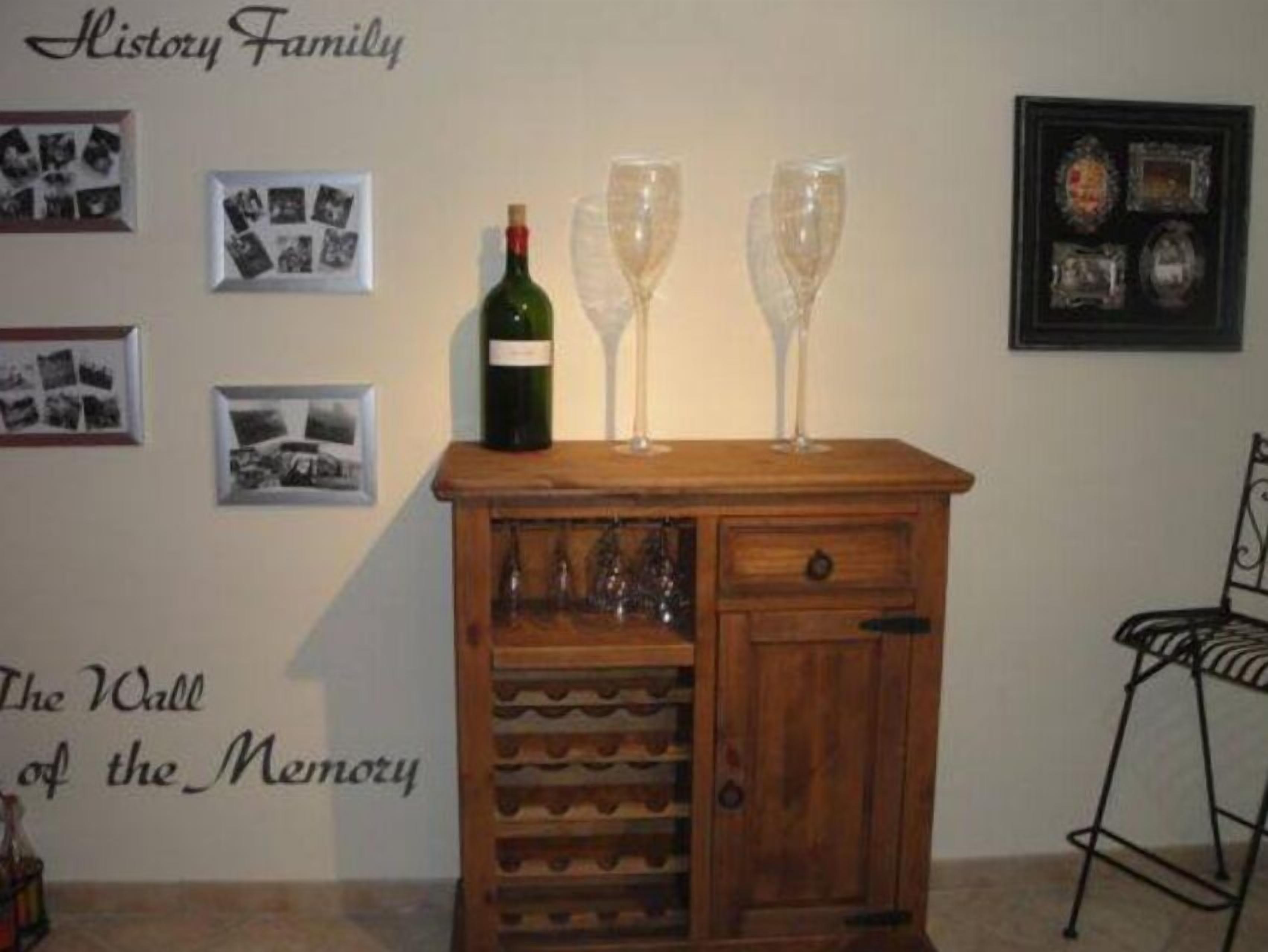 A wooden cabinet with wine glasses and a bottle on top, a wall with framed photos, and a sign reading "The Wall of the Memory".