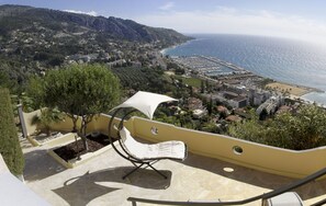 A balcony with a white chair and umbrella, overlooking a coastal town with a beach and marina. - Magnificent villa in a spectacular setting with 360° views of the Mediterranean  (Menton)