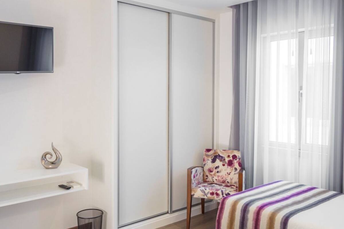 Habitación de hotel con dos camas, televisor montado en la pared, una silla, mesita de noche y puerta corredera.