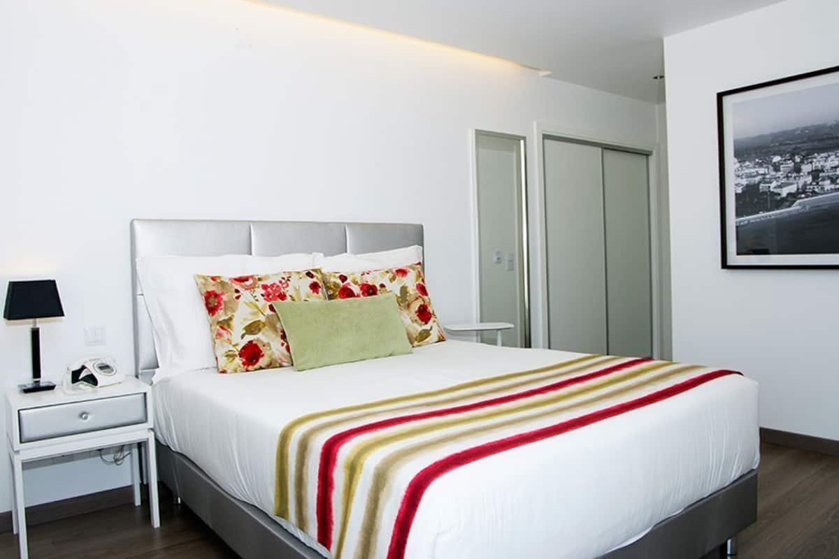 Un dormitorio ordenado con cama, mesita de noche, lámpara y un cuadro en la pared.