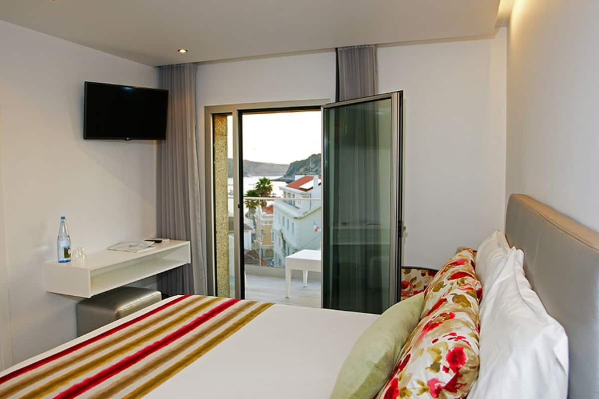 Habitación de hotel con cama, televisor de pantalla plana, escritorio con botella y vasos, y vista al exterior.