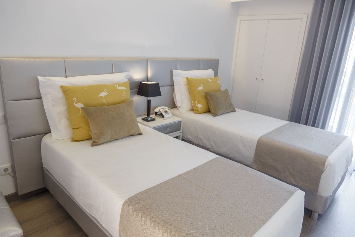 Habitación de hotel con dos camas, una mesita de noche con lámpara y teléfono, y una puerta.