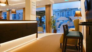 A hotel reception area with a reception desk, seating area, and a view of the street outside. - Hotel Concha (Alcobaça)