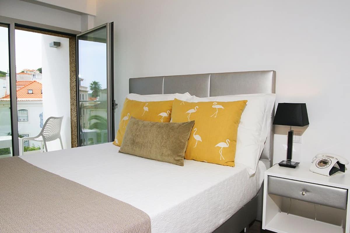 Habitación de hotel con cama, mesita de noche, lámpara y vistas al exterior.