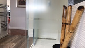 A modern bathroom with a glass shower enclosure, a bamboo plant, and a white tiled wall.