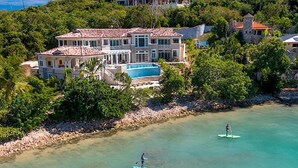 Una casa grande con piscina, rodeada de exuberante vegetación y un mar azul cristalino.