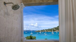 Un baño con ducha y vistas a barcos en un mar azul.