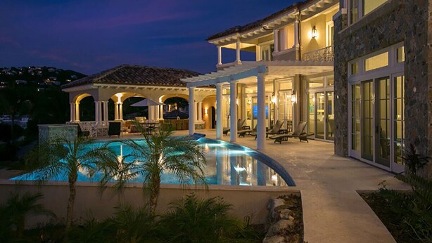 Una casa grande con piscina, mobiliario exterior y un patio cubierto.