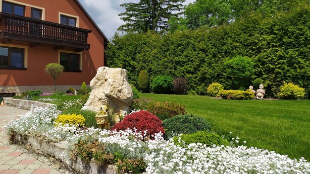 A house with a balcony, surrounded by a well-maintained garden with various plants and flowers. - Apartmány OKOUN (Velke Losiny)