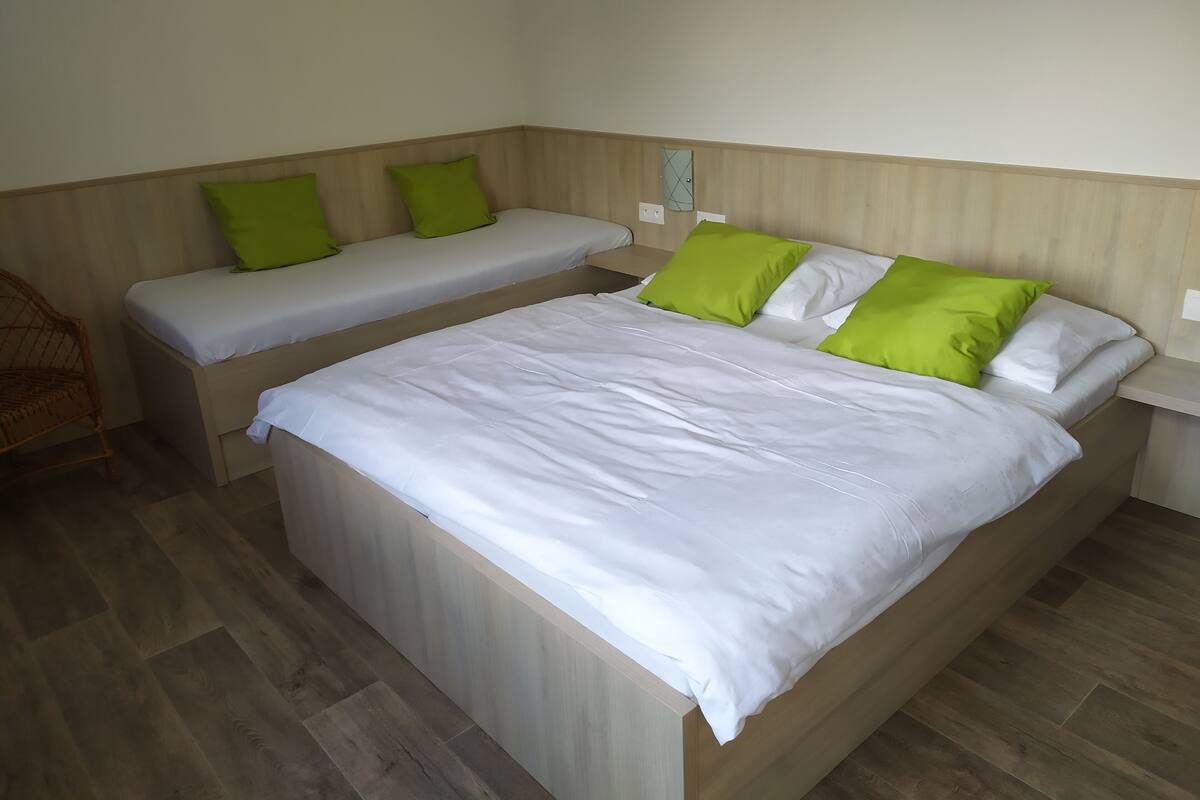 A room with a large bed and two smaller beds, all with white bedding and green pillows.