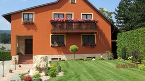 A two-story house with a balcony, stone steps, and a well-maintained garden. - Apartmány OKOUN (Velke Losiny)