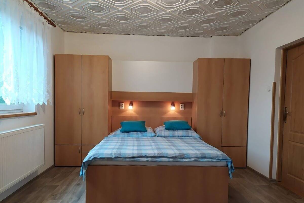 A bedroom with a bed, wooden wardrobe, and a ceiling with a geometric pattern.