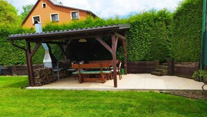 A wooden pergola with a table and benches in a backyard. - Apartmány OKOUN (Velke Losiny)