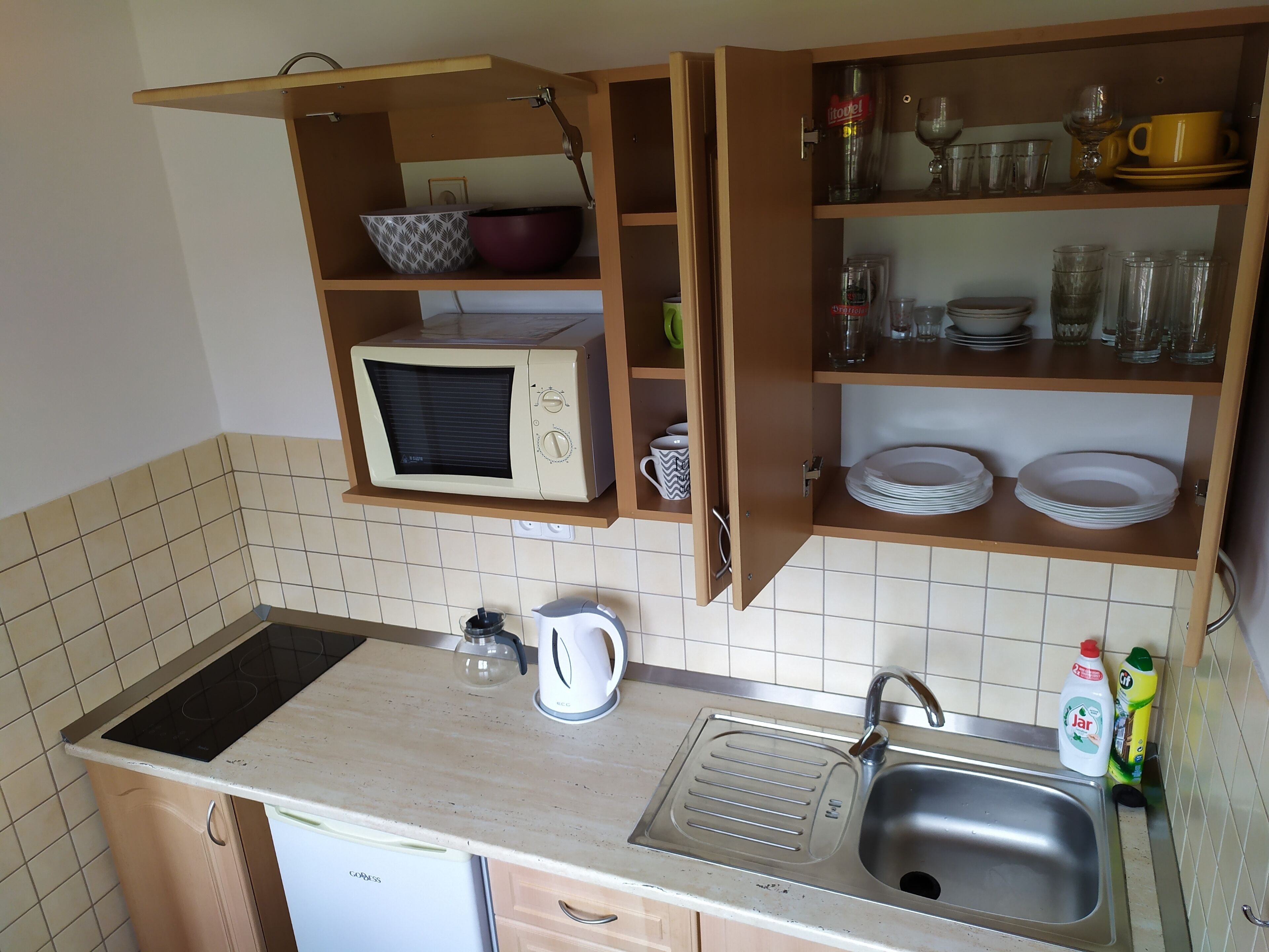 Een kleine keuken met een magnetron, spoelbak en opslagplanken.