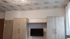 A room with a TV mounted on a wall, wooden cabinets, and a ceiling with a geometric pattern. - Apartmány OKOUN (Velke Losiny)