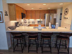 A modern kitchen with wooden cabinets, a stainless steel refrigerator, a built-in oven, and a large island with bar stools. - Snowcreek Resort Vacation Rental 848 (Mammoth Lakes)
